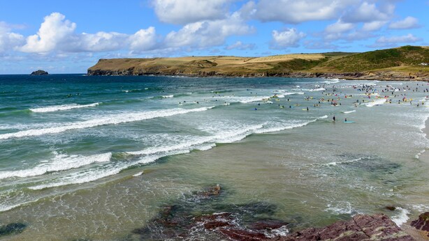 A beach with waves, a rocky shoreline, and a hilly landscape in the background. - High Tide (Wadebridge)