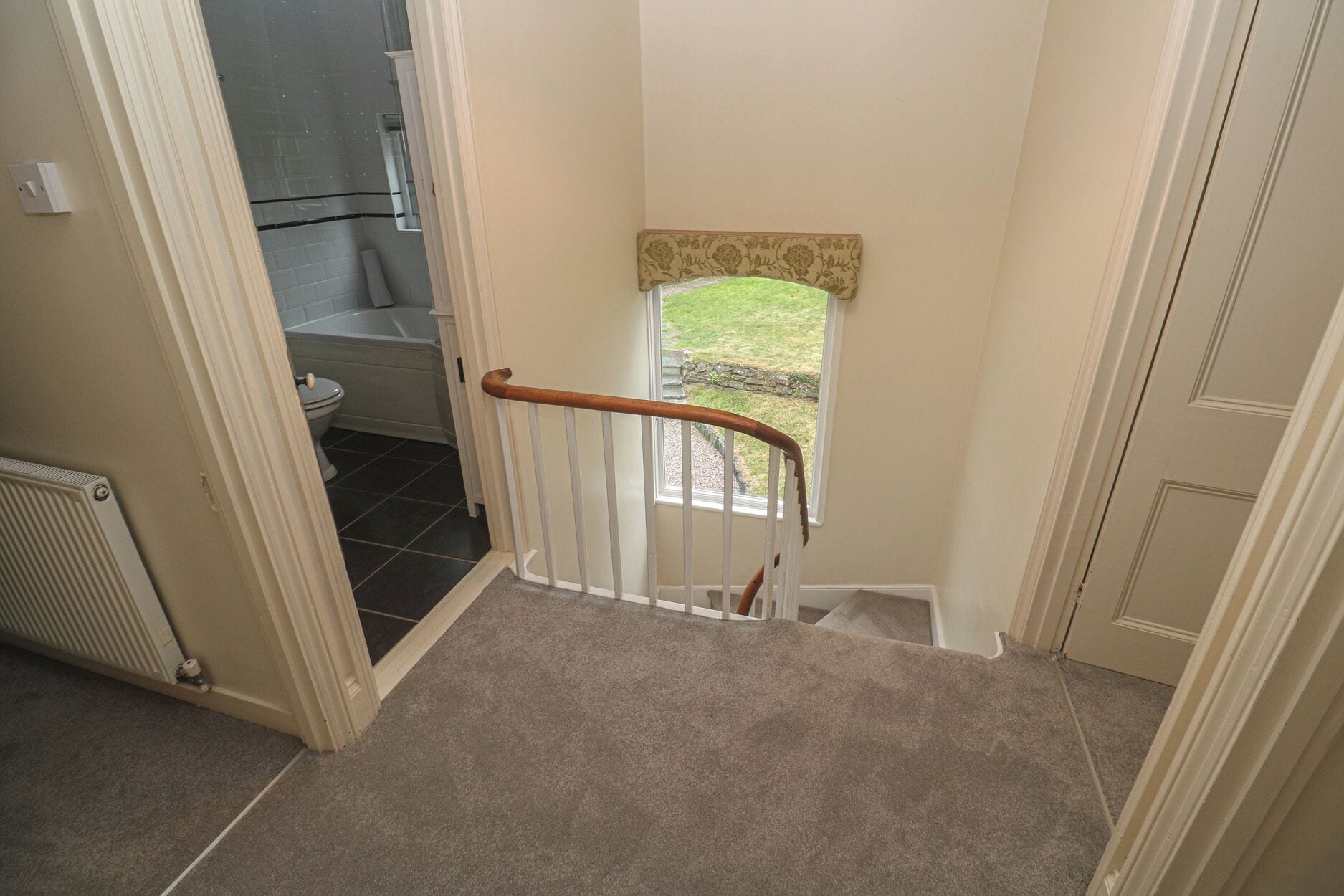 A staircase with a wooden handrail leading to a door with a small window.