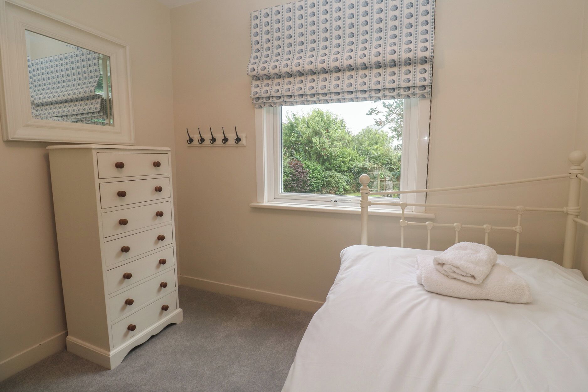 A bedroom with a bed, a dresser, a window with a view of greenery, and a mirror on the wall.