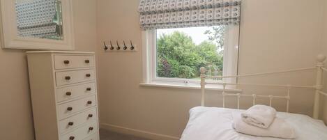 A bedroom with a bed, a dresser, a window with a view of greenery, and a mirror on the wall.