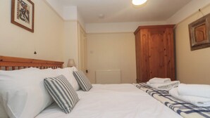 Un lit bien fait, avec du linge de lit blanc et des oreillers à rayures, une tête de lit en bois, un radiateur et une armoire en bois.