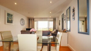 Ein modernes Wohnzimmer mit einem Glastisch, umgeben von weißen Stühlen, einem Sofa und einem großen Fenster mit Blick.