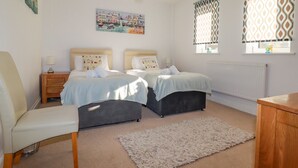 Ein Schlafzimmer mit zwei Betten, einem Sessel, einem Nachttisch, einer Heizung und einem Fenster mit gemusterten Vorhängen.