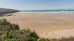 Ein weiter Sandstrand mit sanften Wellen, blauem Himmel und etwas Vegetation im Vordergrund.