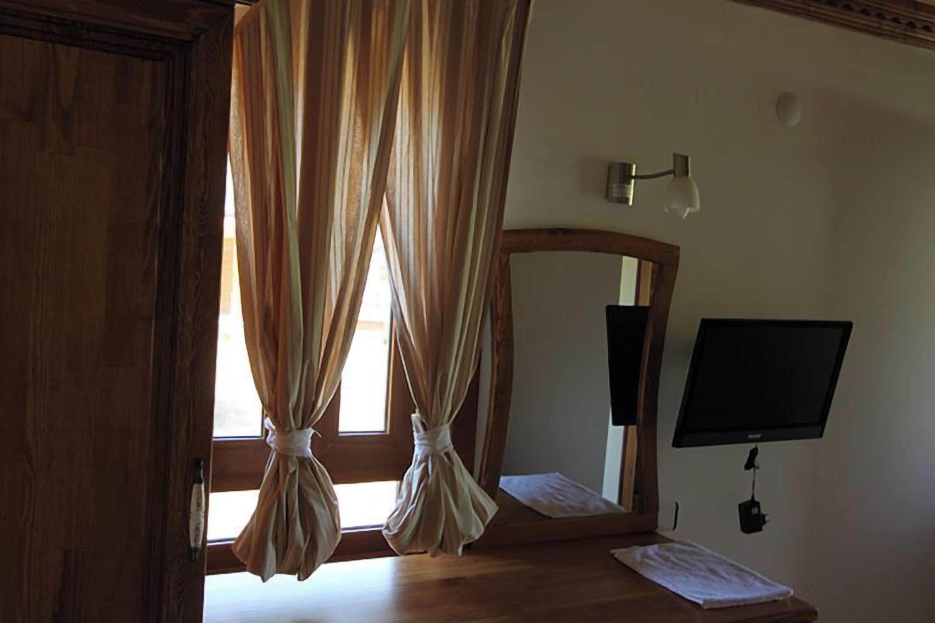 Una habitación con piso de madera, un espejo grande, un televisor de pantalla plana y cortinas atadas en la parte superior.