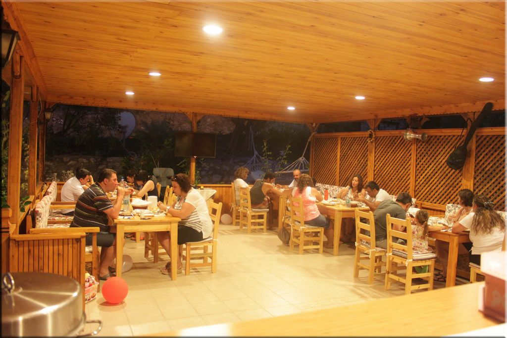 Un espace de restauration doté d’un toit en bois, avec des tables et des chaises, entouré d’un mur de pierre et de verdure.