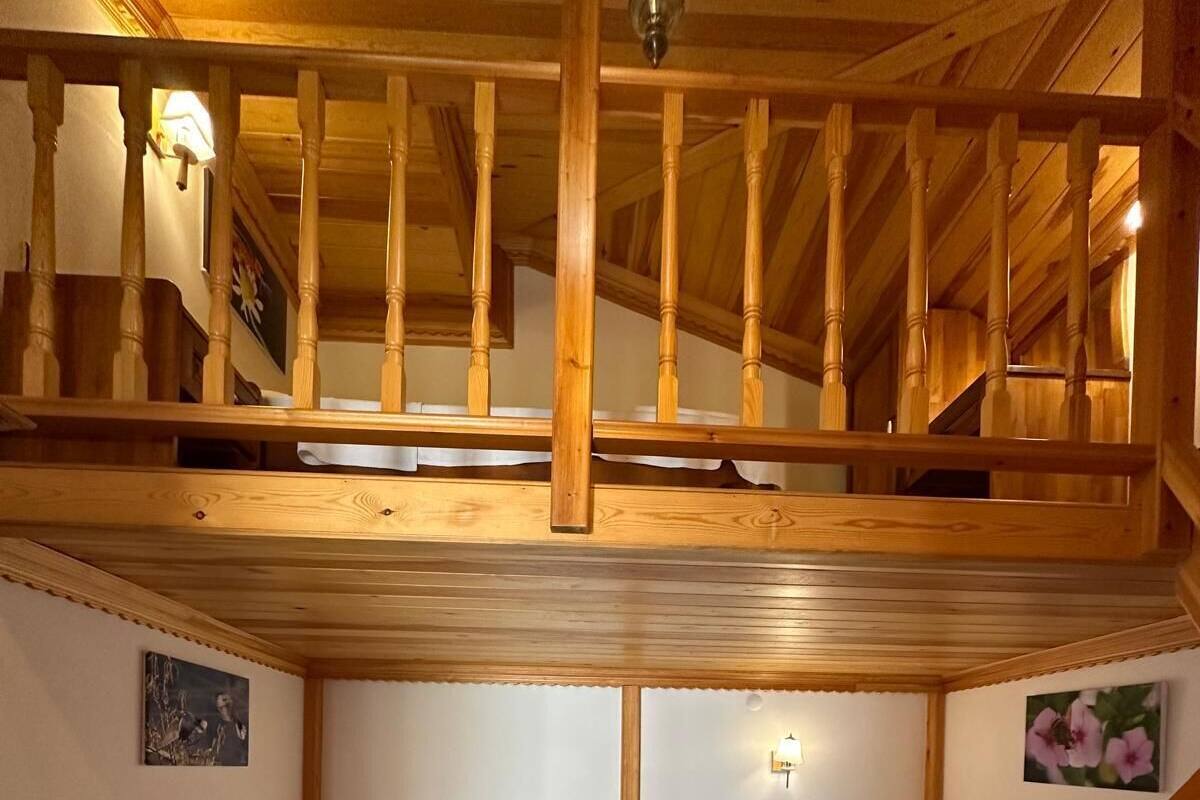 Una habitación con dos camas individuales, vigas de madera, una escalera y una pequeña mesa.