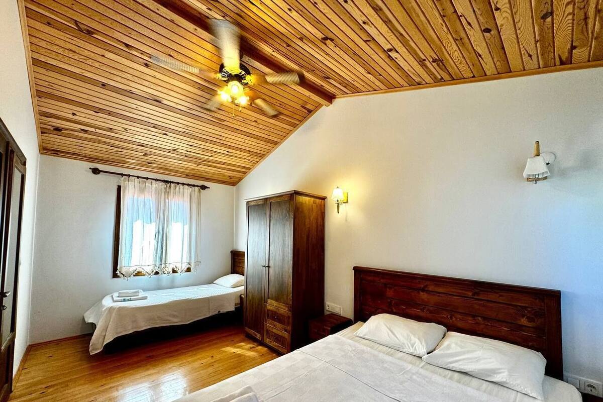 Un dormitorio con techo de madera, cama con ropa de cama blanca, mesita de noche y armario.