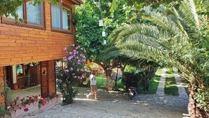 A wooden house with a porch, surrounded by lush greenery and flowering plants. - Elly's Home (Datça)
