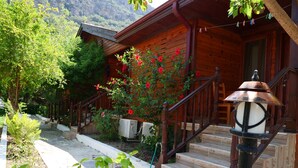 A wooden house with a wooden staircase leading to a porch, surrounded by greenery and a mountain backdrop. - Elly's Home (Datça)