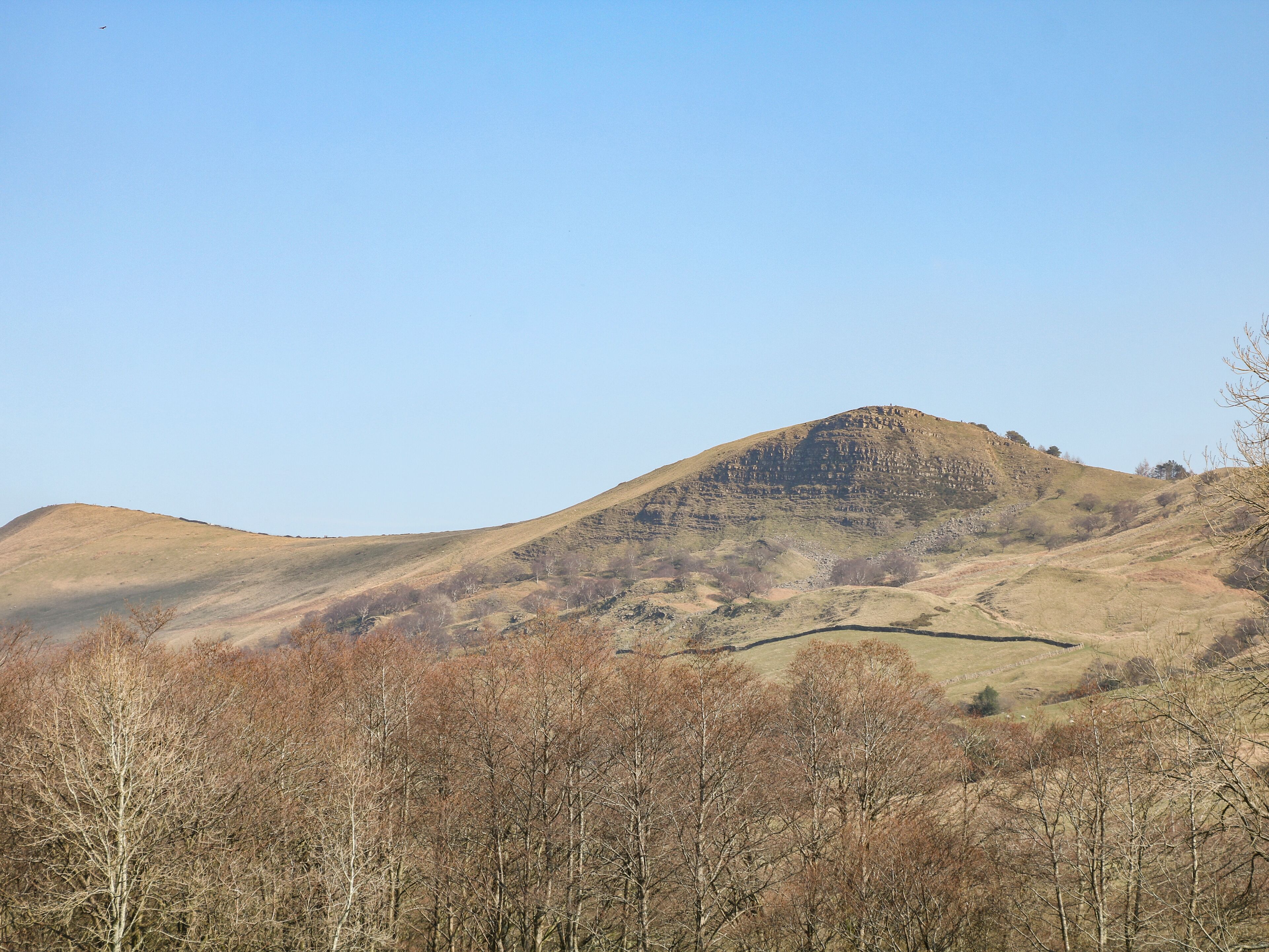 Eine gebirgige Landschaft mit einem markanten Hügel und vereinzelten Bäumen im Vordergrund.