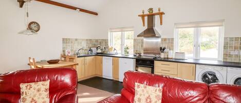 A kitchen with a dining area, red leather sofas, and a hanging clock.