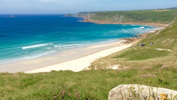 A coastal landscape with a sandy beach, grassy terrain, and a clear blue sea. - 14 Boscaswell Downs (Penzance)