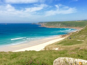 A coastal landscape with a sandy beach, grassy terrain, and a clear blue sea. - 14 Boscaswell Downs (Penzance)