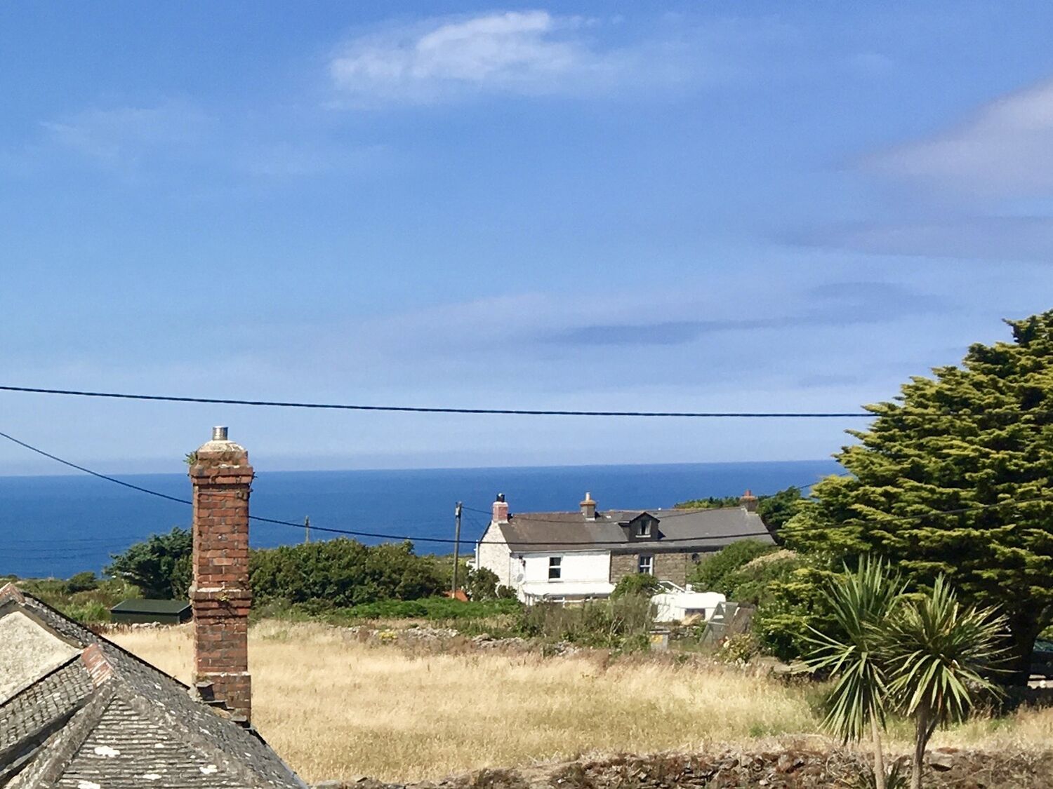 Vista costera con una chimenea de ladrillo, una casa blanca y un árbol en primer plano.
