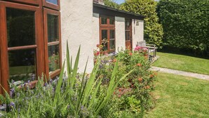 Una casa con amplios ventanales, un muro de piedra y un jardín bien cuidado con diversas plantas y flores.