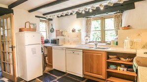Cocina compacta con refrigerador, microondas y lavavajillas, gabinetes de madera, piso de losetas de piedra y una ventana con cortinas.