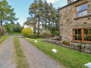 A stone house with a gravel driveway leading to a metal gate. - Moorgair Cottage (Hexham)