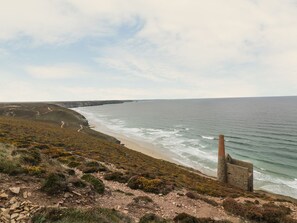Un paysage côtier avec une plage rocheuse, une falaise et une construction en pierre surplombant la mer.