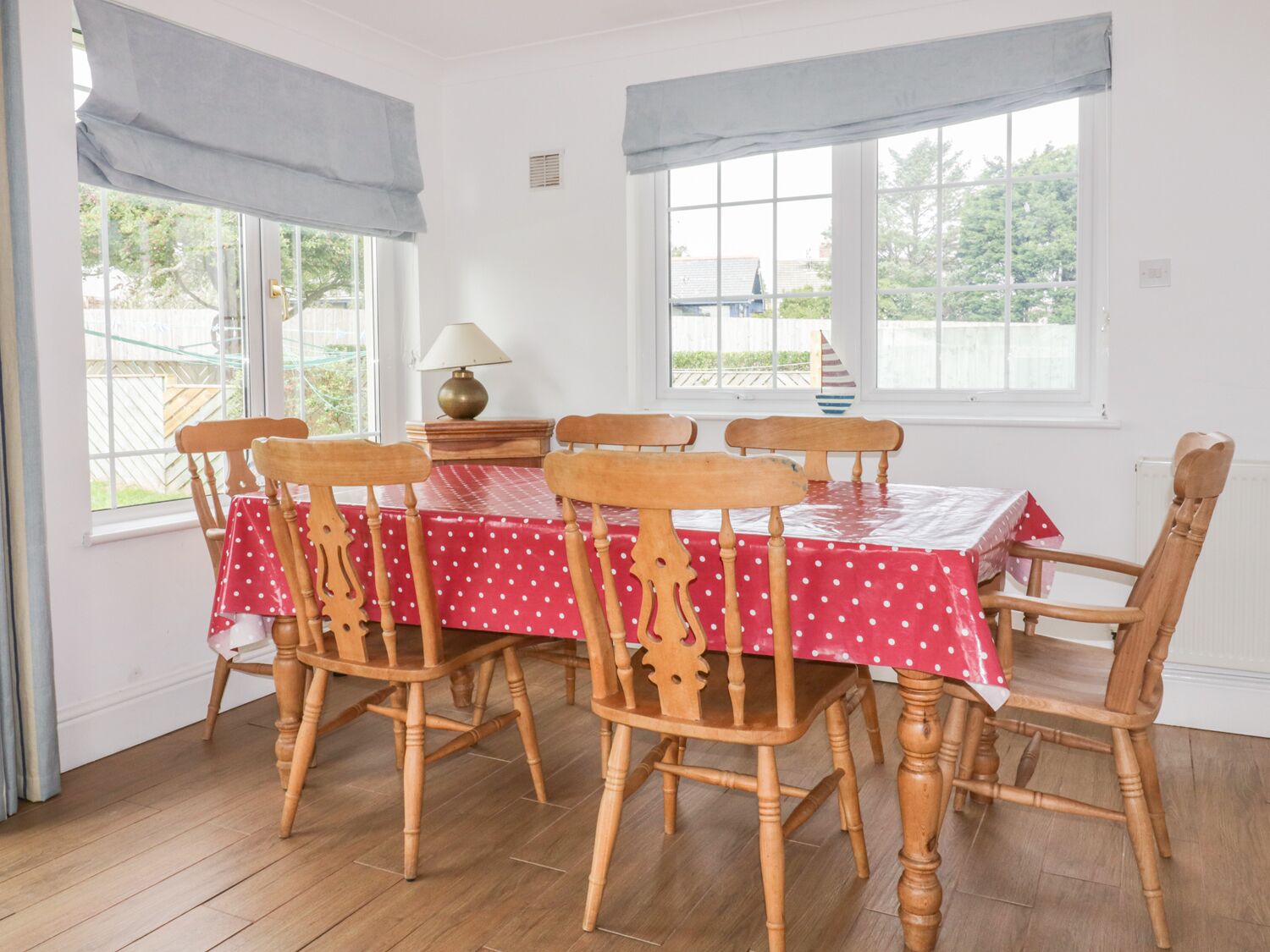 A dining area with a wooden table and chairs, covered with a red tablecloth.