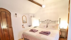 Une chambre avec une armoire en bois, un lit recouvert d’un tapis rouge et un miroir au mur.