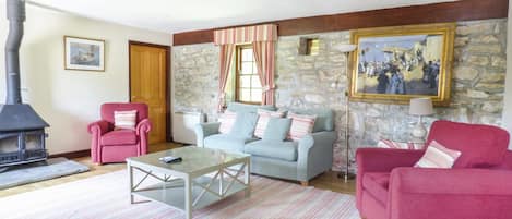 A cozy living room with a stone wall, a fireplace, two sofas, and a red armchair.