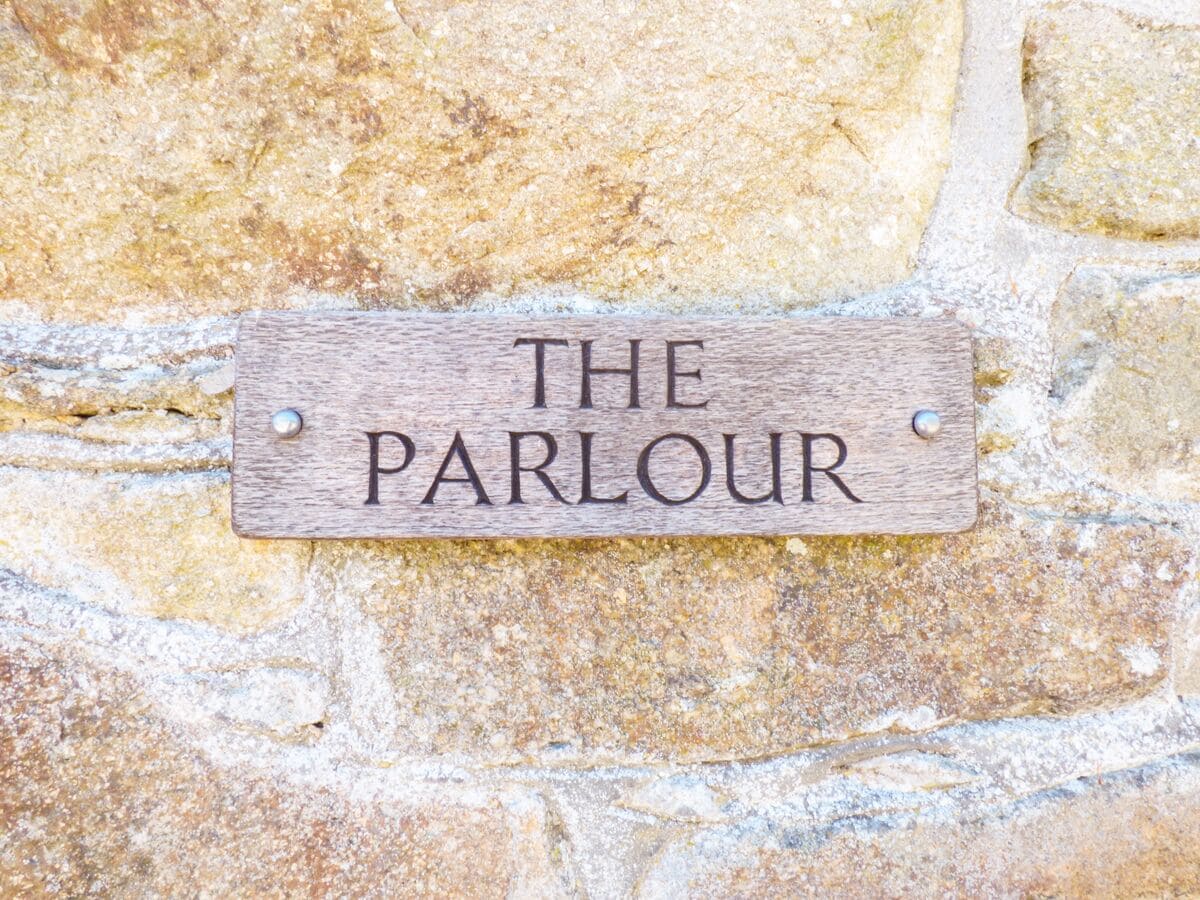 A wooden sign with the text "THE PARLOUR" mounted on a stone wall.