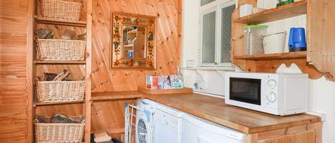 A compact kitchen with wooden cabinetry, a washing machine, a microwave, and wicker baskets.