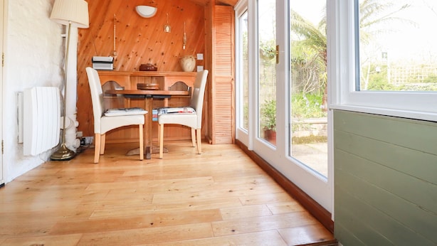 Een kamer met houten lambrisering, een eettafel met stoelen, grote ramen en een radiator.