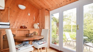 Een houten interieur met een ronde tafel, twee stoelen, een radio en uitzicht op de tuin via een schuifdeur met glas.