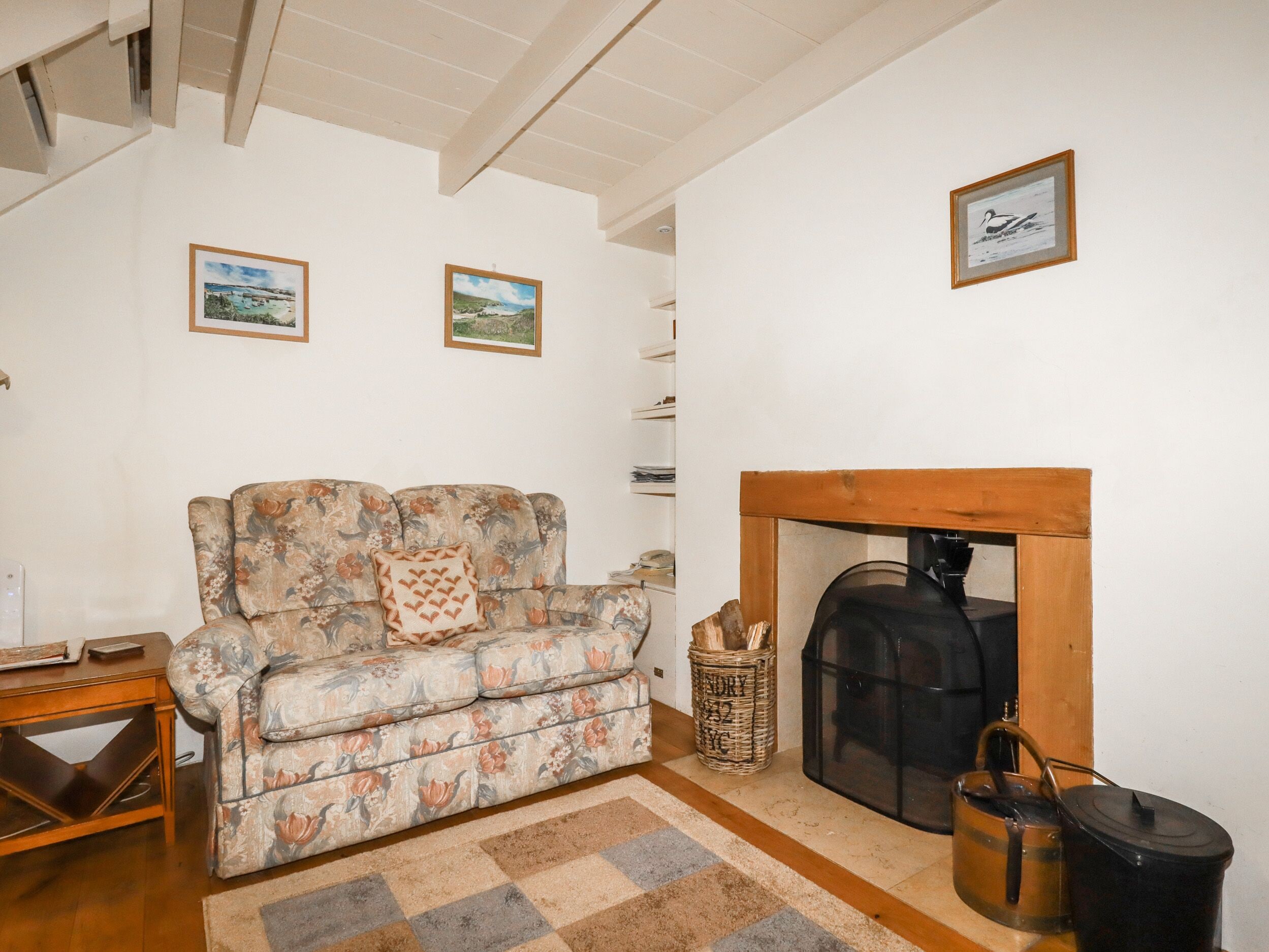 A living room with a floral sofa, a fireplace, and two framed pictures on the wall.
