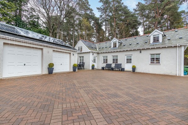 A large, white building with multiple garage doors and a paved courtyard. - Dunstaffnage Cottage (Grantown-on-Spey)