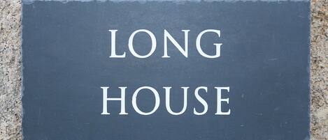 Een donkergrijze bord met de woorden 'LONG HOUSE' in witte, hoofdletters.