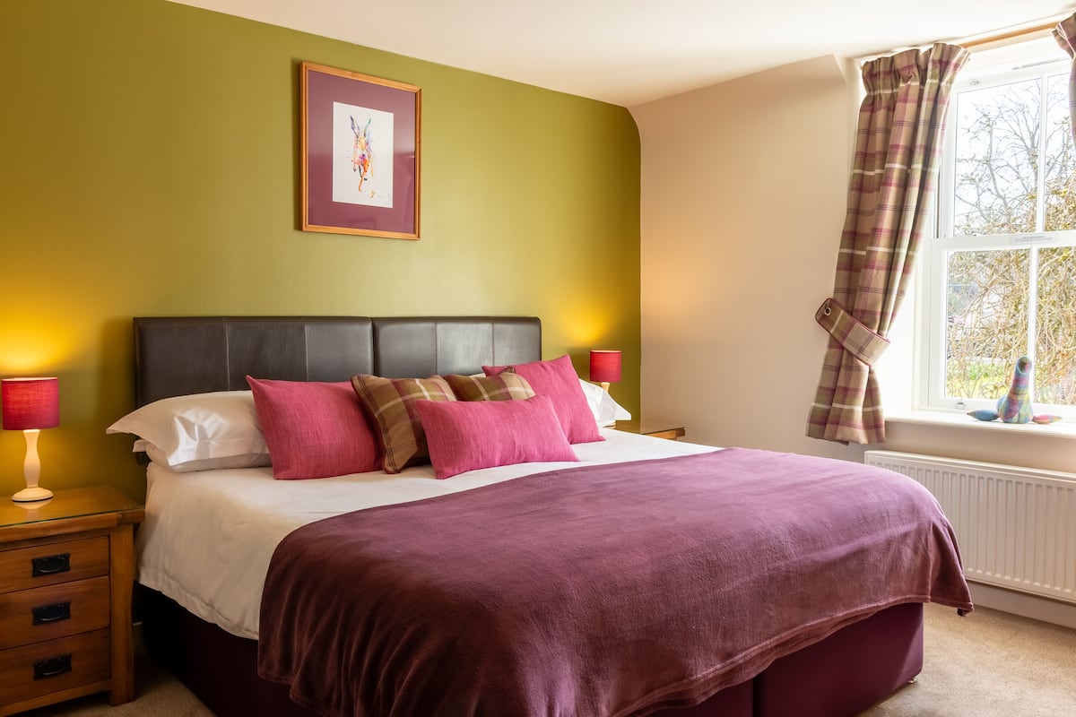 A bedroom with a bed, nightstands, a window with curtains, and a framed picture on the wall.