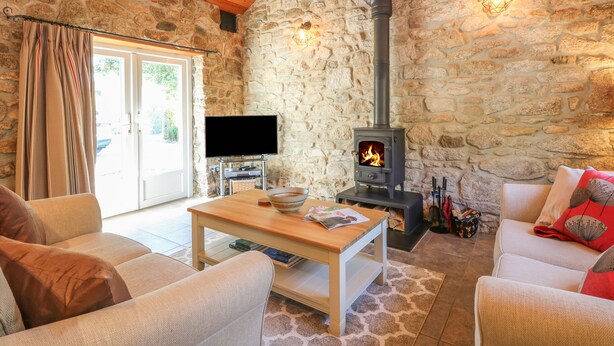 Un salón acogedor con pared de piedra, techo de madera, chimenea, televisor y asientos cómodos.