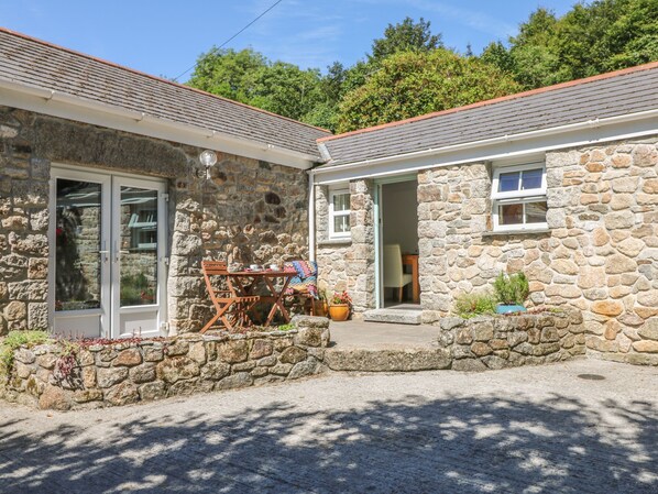 A stone house with a patio, a table, and chairs. - Pond Cottage (Truro)