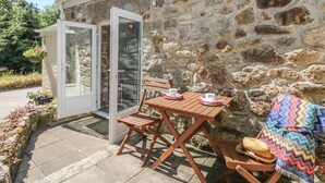 Un edificio de piedra con un escaparate de vidrio que da a un patio con una mesa y sillas de madera.