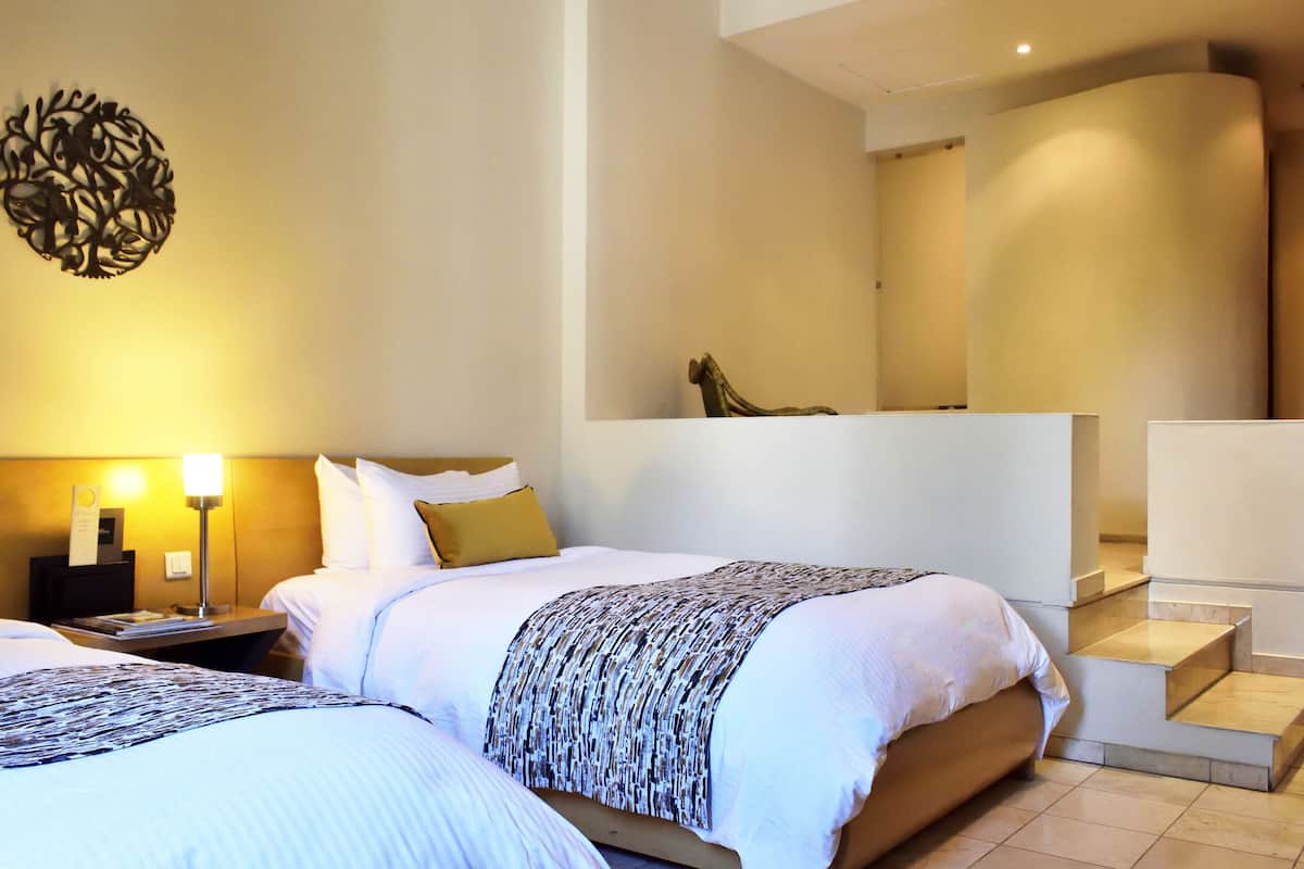 A hotel room with two beds, a nightstand, a lamp, and a staircase.