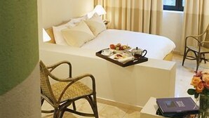 Hotellihuone, jossa on sänky, tuoli, hedelmävati ja ikkuna.