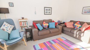 A living room with two sofas, a chair, a bookshelf, and a colorful rug. - Kernow Cottage (Helston)