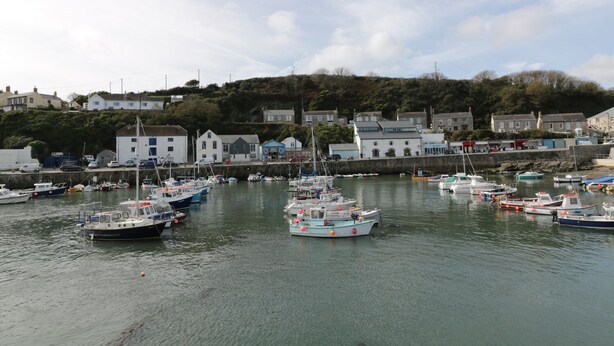 A harbor with multiple boats docked, surrounded by buildings and a hillside in the background. - Kernow Cottage (Helston)