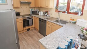A kitchen with wooden cabinets, a microwave, a sink, and a window with a view. - Kernow Cottage (Helston)