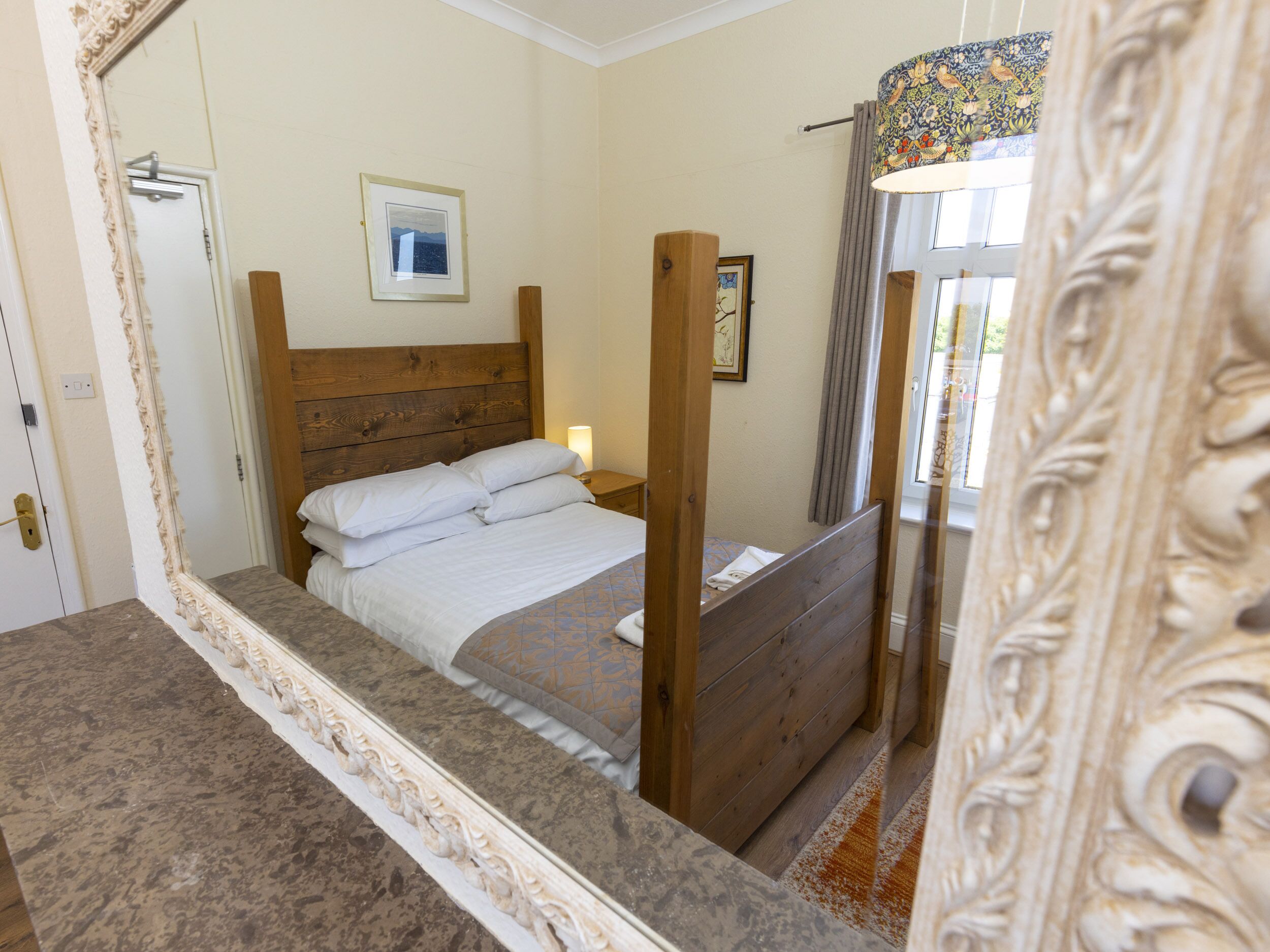 A bedroom with a wooden bed, a nightstand, a framed picture on the wall, and a window with curtains.