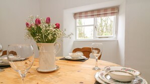 A dining table set with white plates, a pitcher of flowers, and wine glasses. - Fleshbeck Cottage (Carnforth)