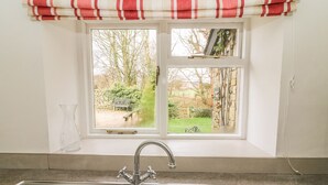 A kitchen with a double sink, a window with a view of a garden, and a red and white striped curtain. - Fleshbeck Cottage (Carnforth)