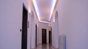 Un pasillo con piso estampado, paredes blancas e iluminación lineal en el techo.