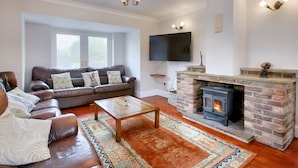 A living room with a leather sofa, a coffee table, a fireplace, and a television mounted on the wall.
