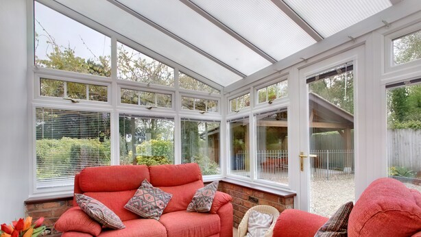 A conservatory with a red sofa set, a wicker chair, and a vase of flowers.