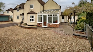 A two-story house with a conservatory, gravel driveway, and a fenced garden area.