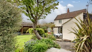 A garden with a patio, a house with a tiled roof, and a tree.